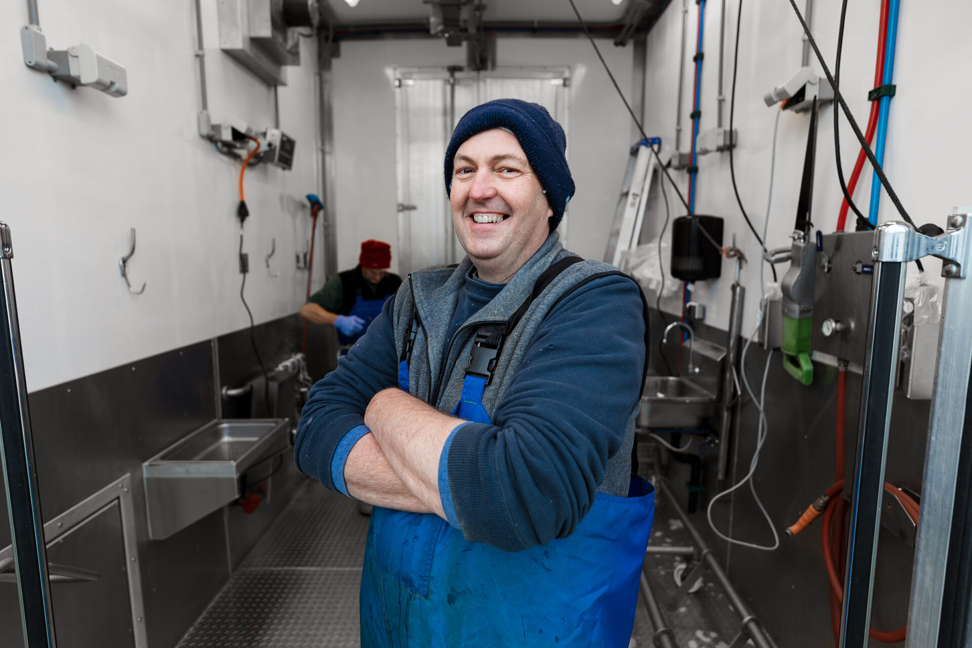 Smiling butcher in blue uniform standing in a Friesla Mobile Meat Harvest Trailer.