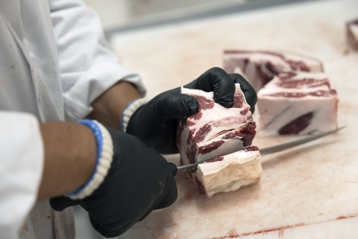 Butcher hand-cutting beef on table.