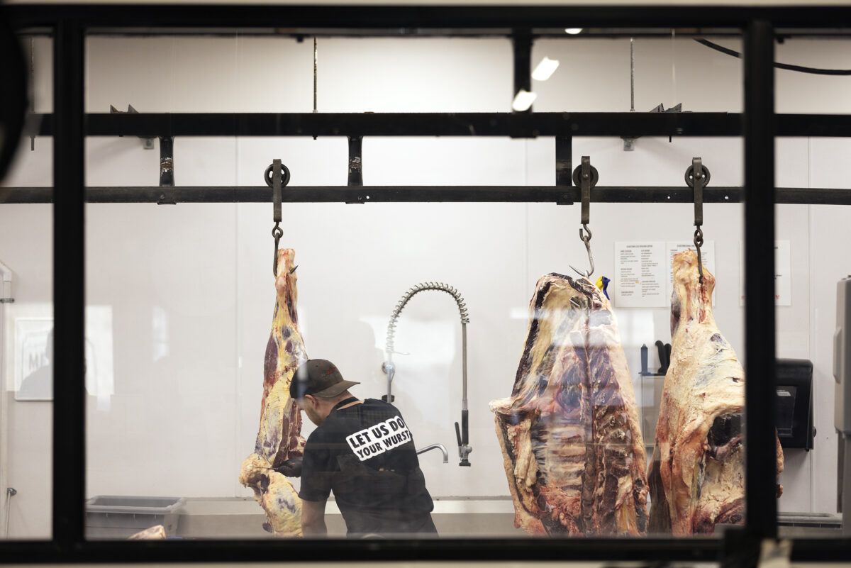 A butcher cuts off a piece of hanging carcass for fabrication.