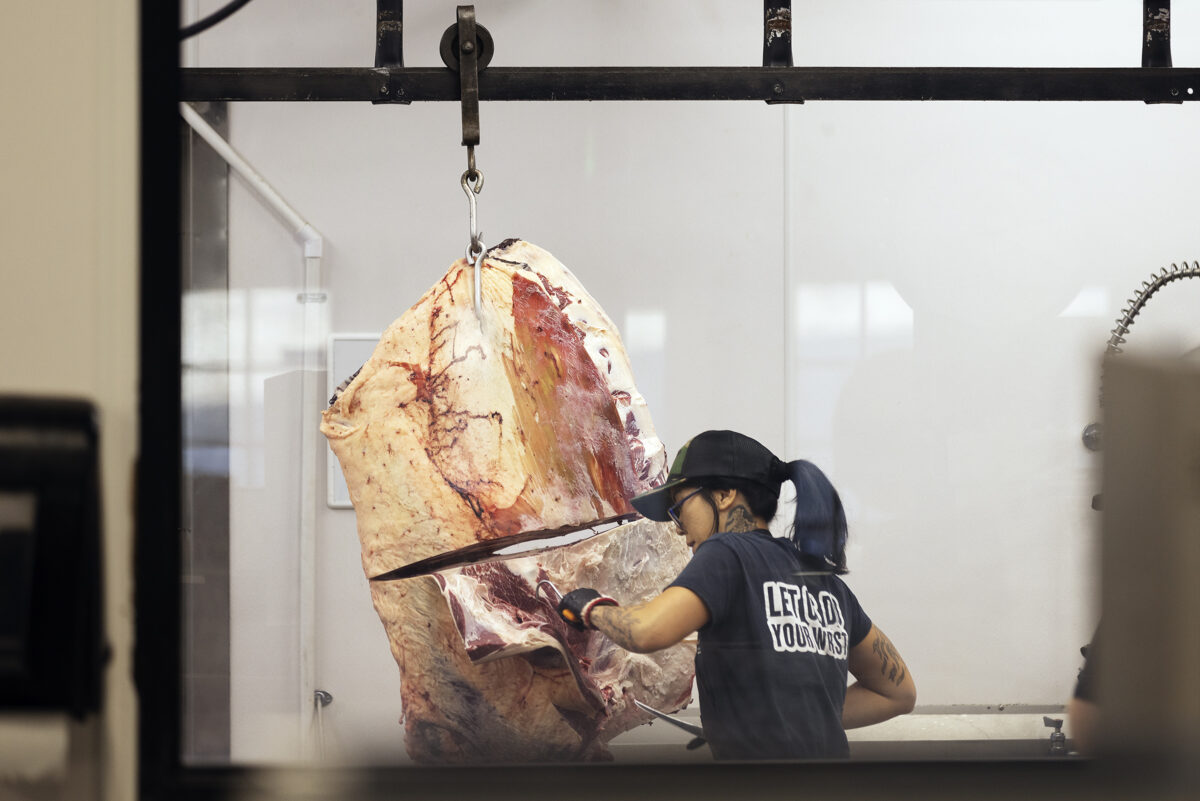 A butcher cuts off a piece of hanging bison carcass for fabrication.