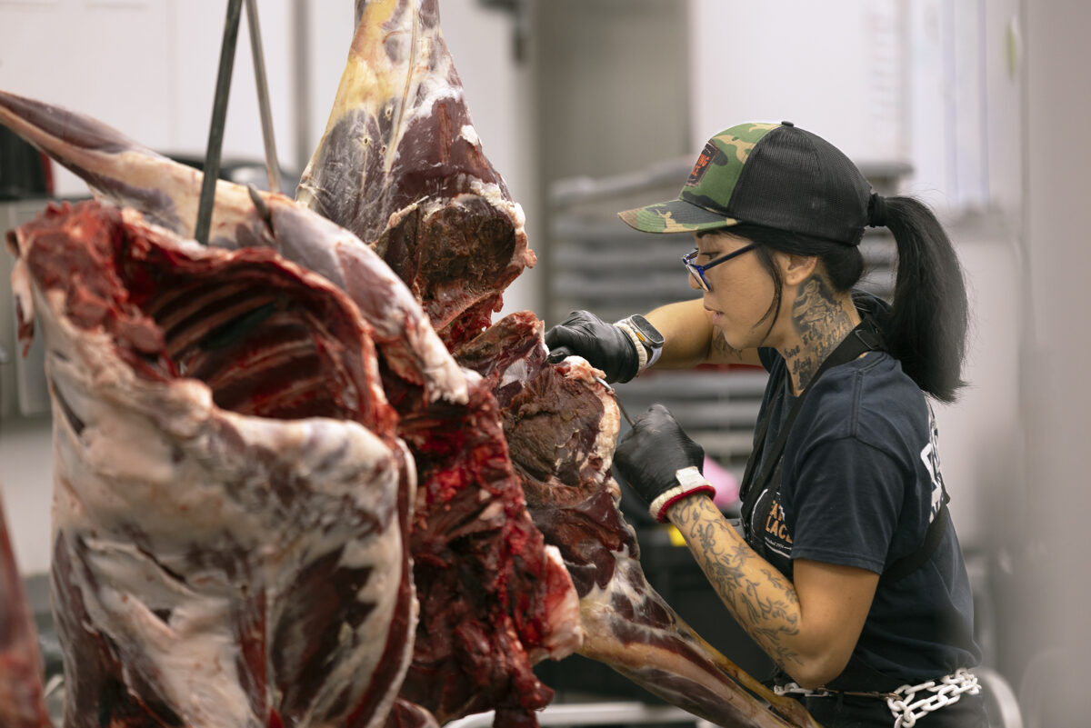 Butcher using knife and hook to cut through animal carcass.