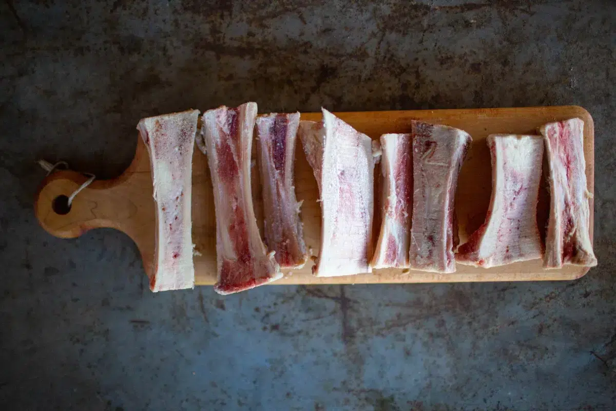 A row of beef marrow bones on a wooden serving paddle.